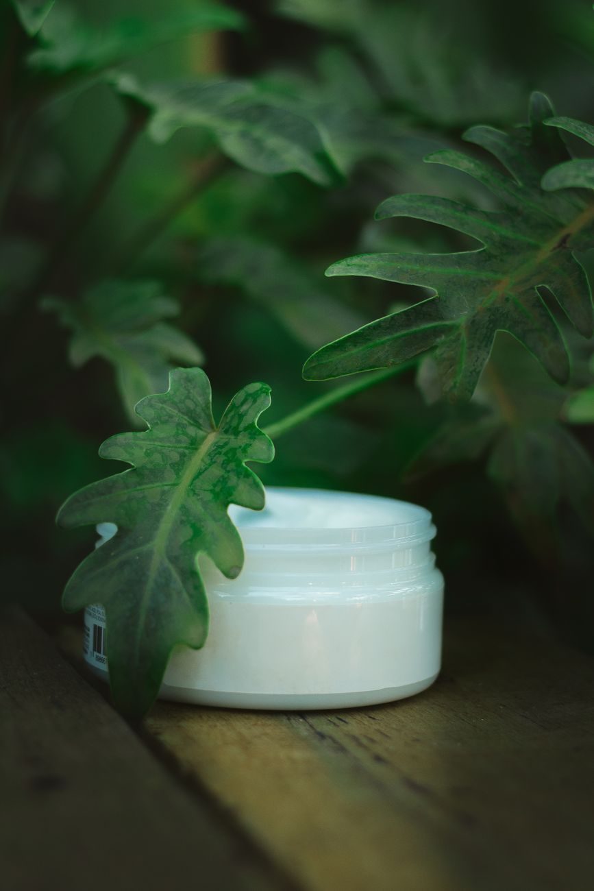 close up of a cream container without a label standing next to a plant